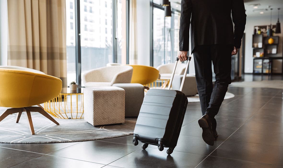 Cropped photo of caucasian businessman wearing suit walking with suitcase in hotel lobby