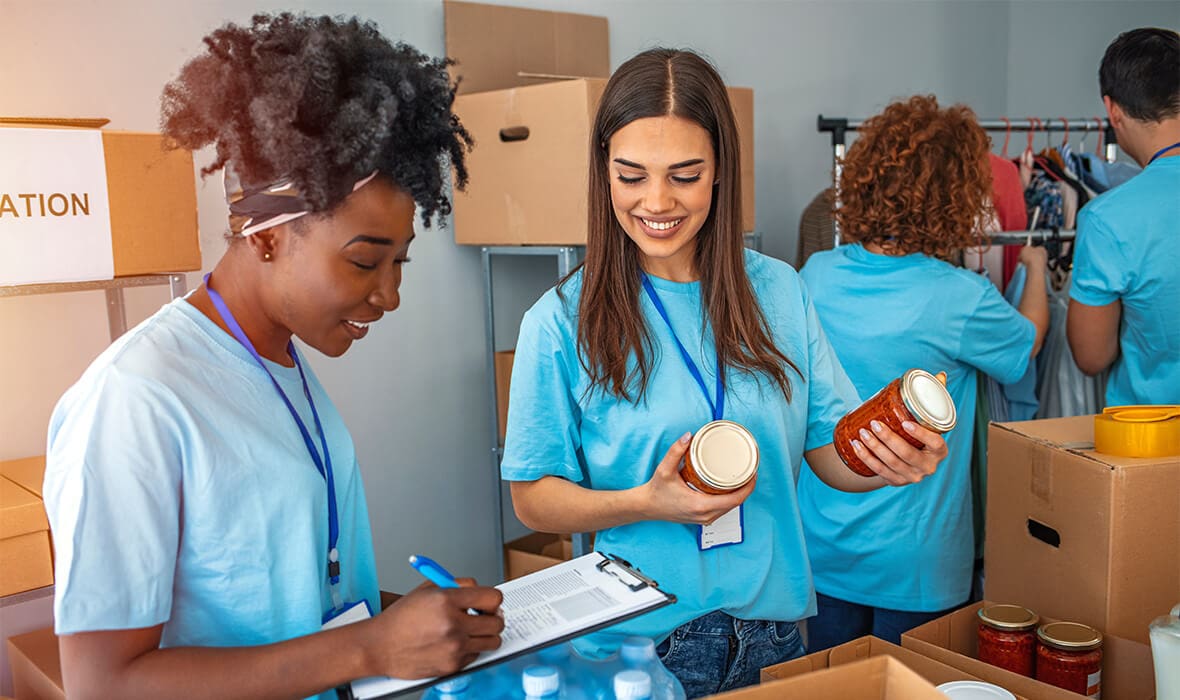 Group of people working in charitable foundation. Happy volunteer looking at donation box on a sunny day. Happy volunteer separating donations stuffs. Volunteers sort donations during food drive