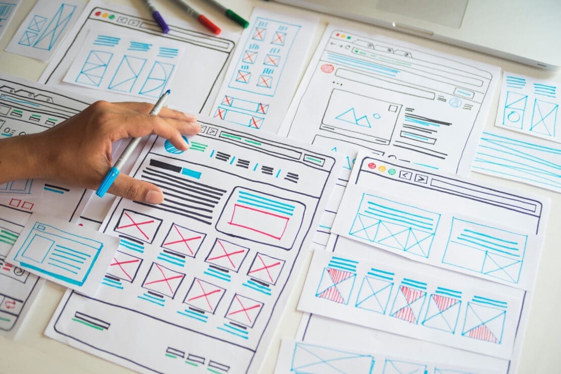 Designer creating website wireframes with hand-drawn sketches for user interface planning and layout ideas.
